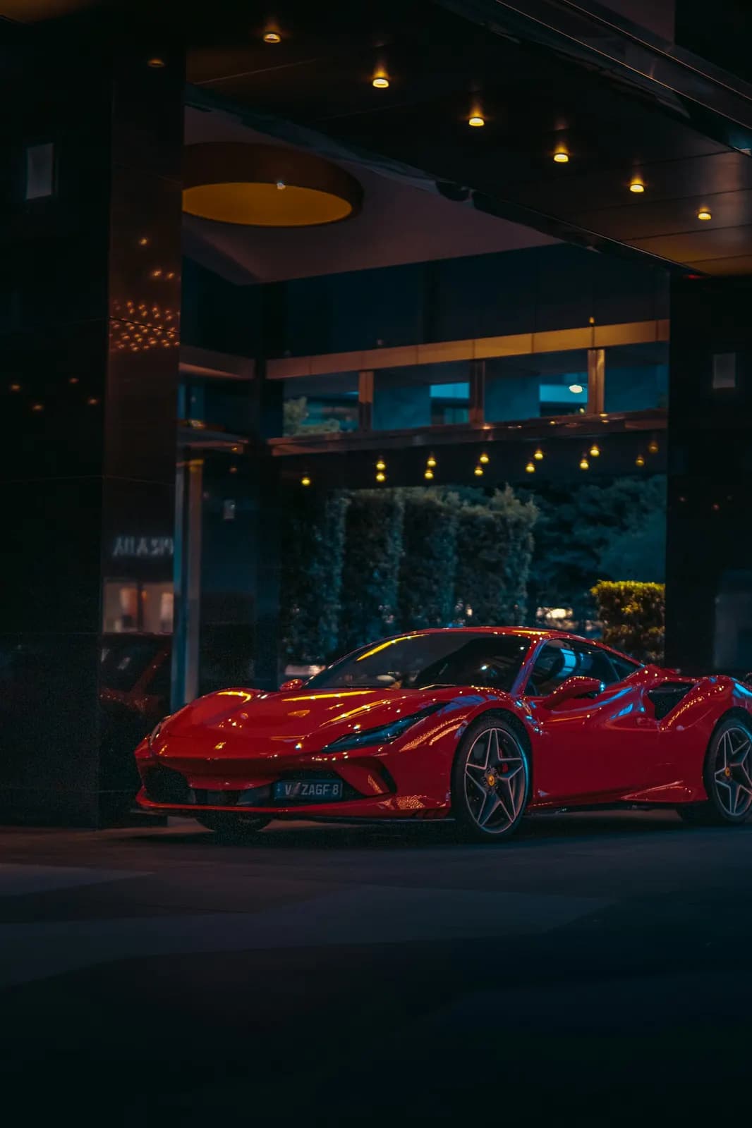 Red Ferrari parked under a lit hotel canopy at night