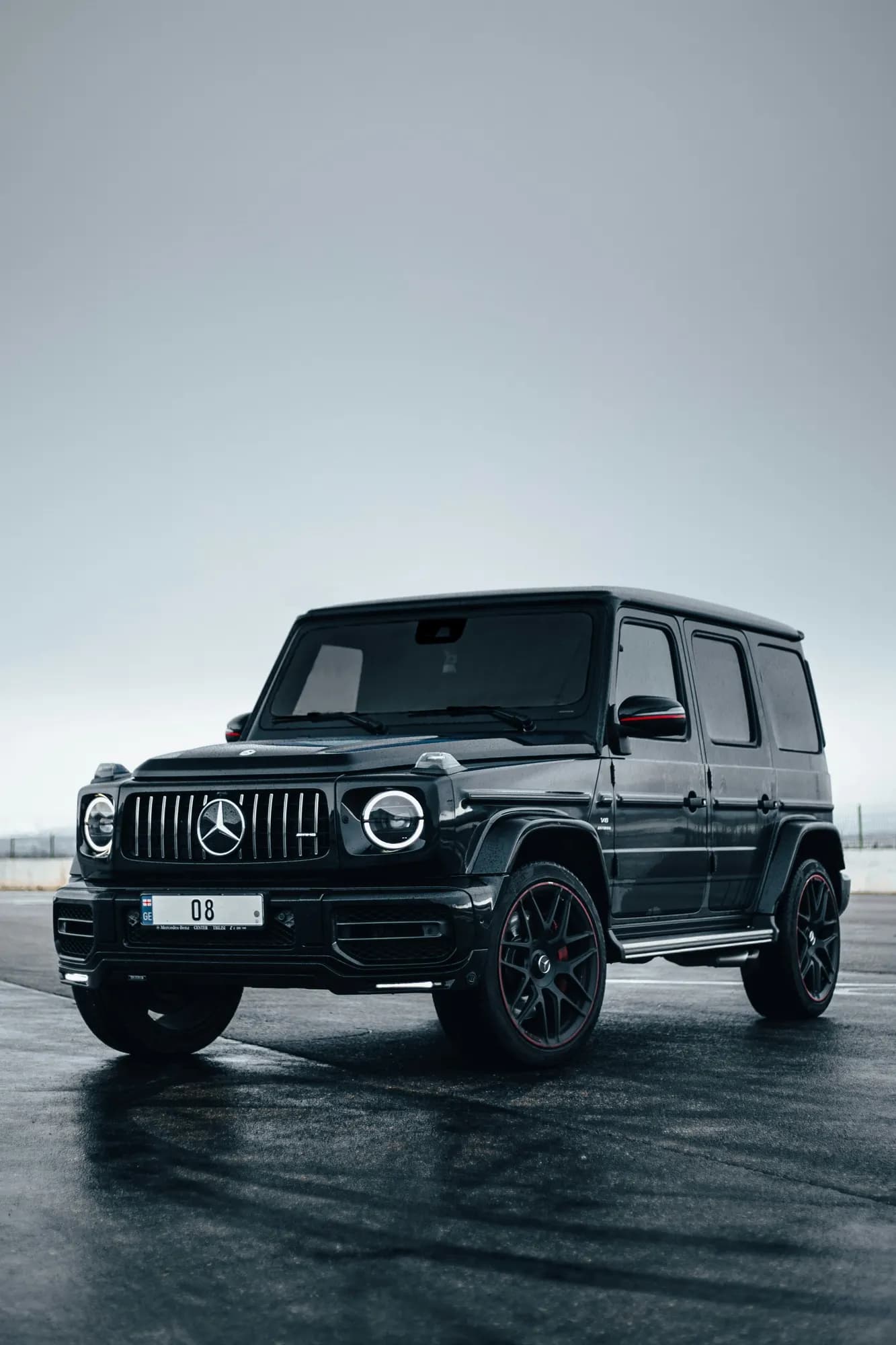 Black Mercedes-AMG G 63 on wet asphalt under a grey sky