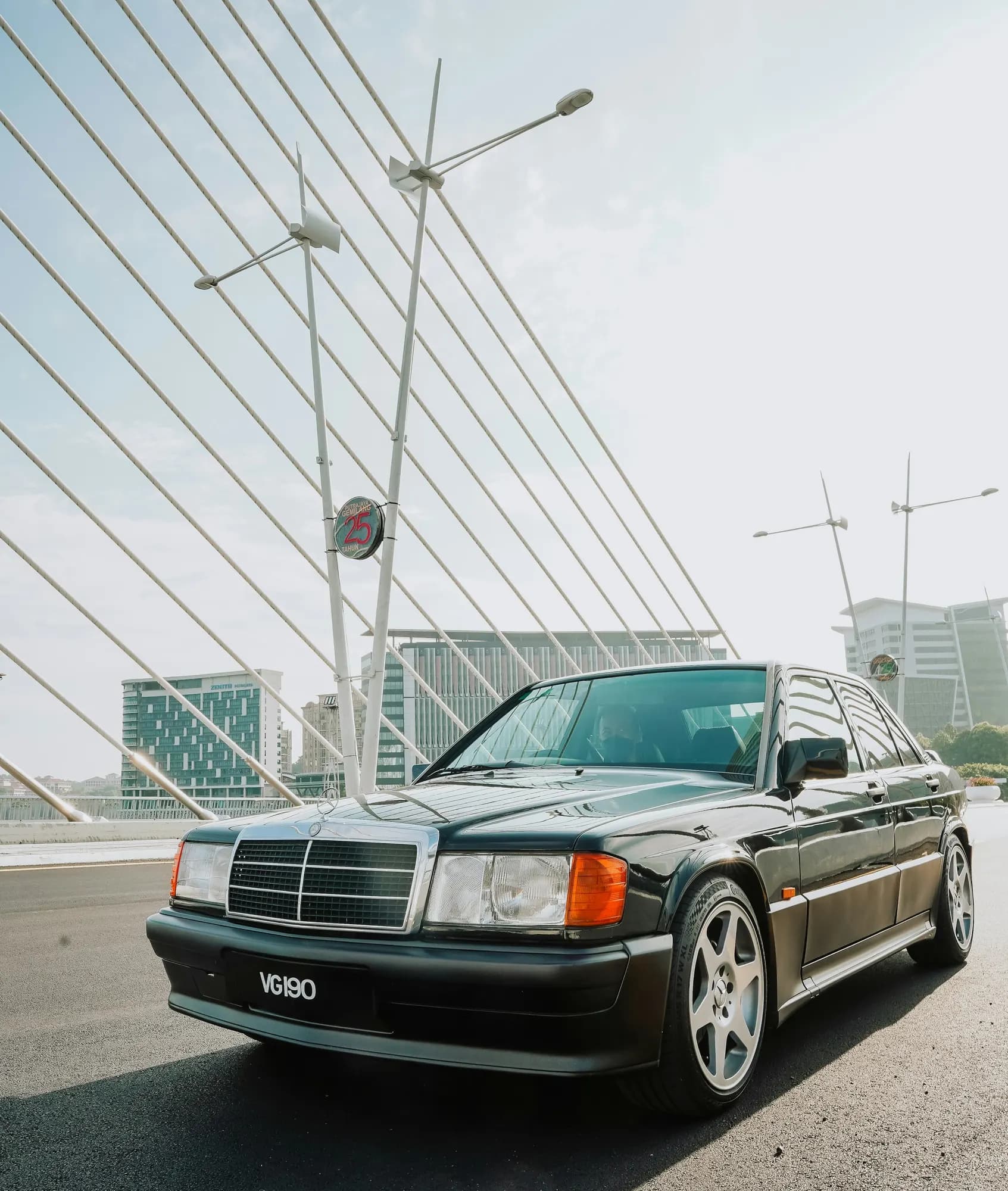 Black Mercedes-Benz 190E on a modern bridge, front three-quarter view