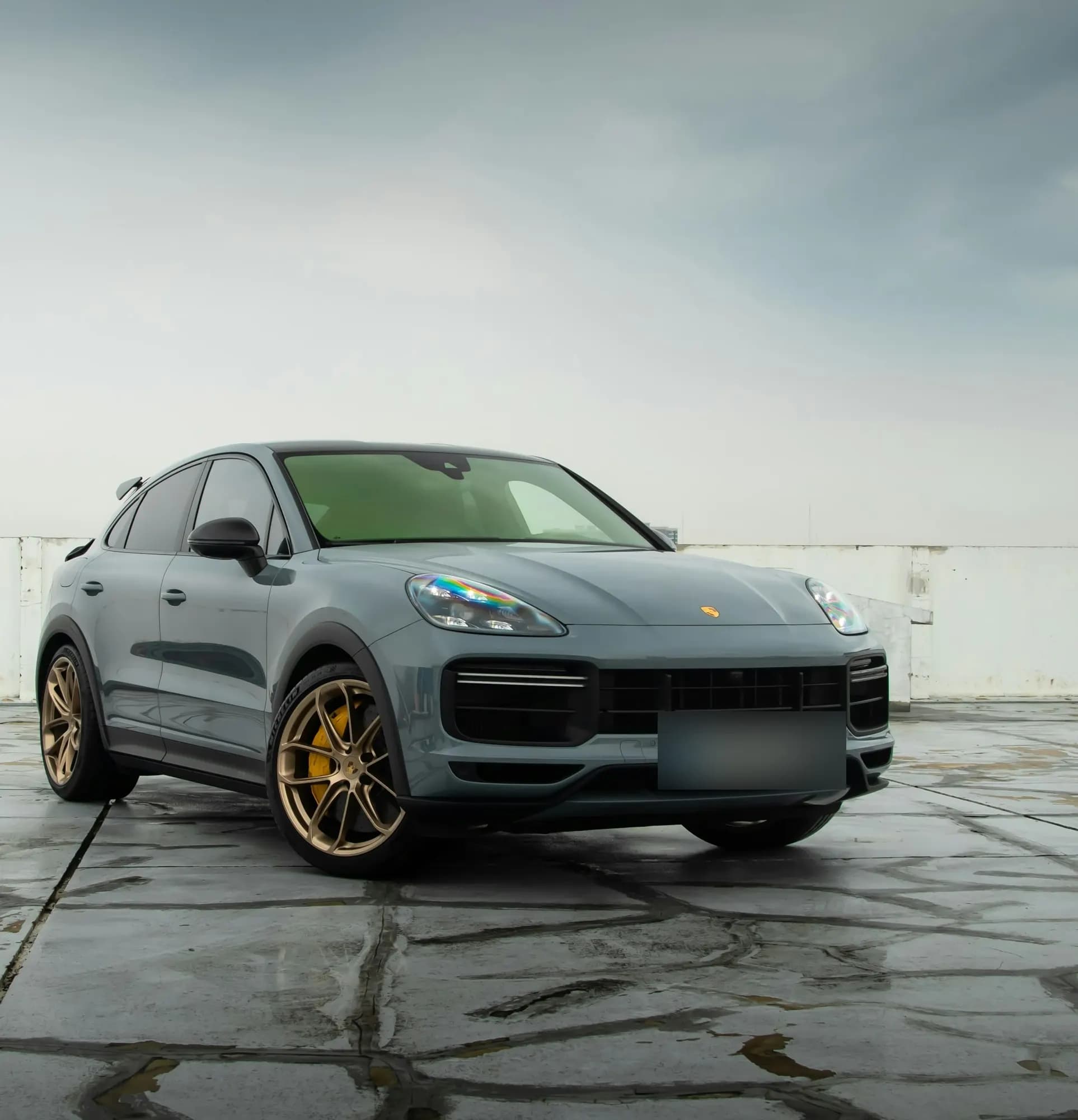 Grey Porsche Cayenne Turbo GT with bronze wheels on wet concrete, front three-quarter view