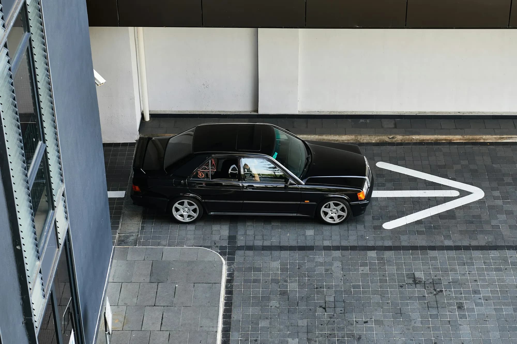 Black Mercedes-Benz 190E seen from above on dark paving