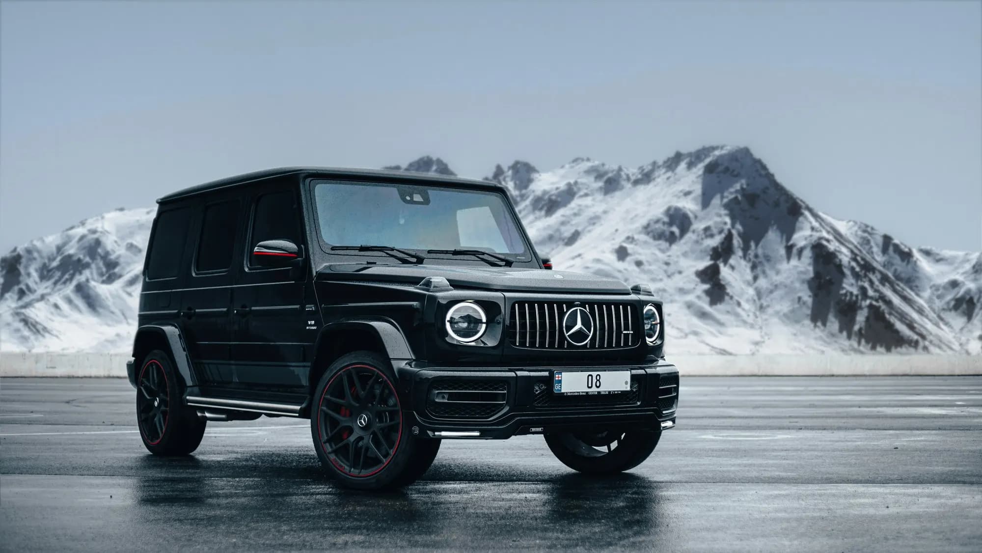 Black Mercedes-AMG G 63 on wet asphalt before snow-covered mountains